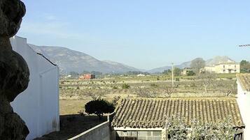 A view of a rural landscape with mountains in the background, a white building with a tiled roof in the foreground, and a red building across the field.
