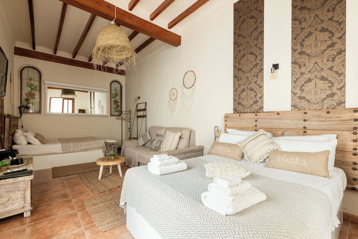 A cozy bedroom with a bed, a sofa, a small table, and a hanging light fixture.