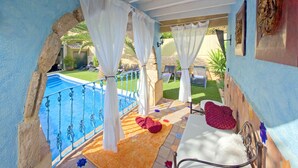 A balcony with a view of a swimming pool, a small table with a chair, and a decorative rug. - Casa Mistela (Jalon)