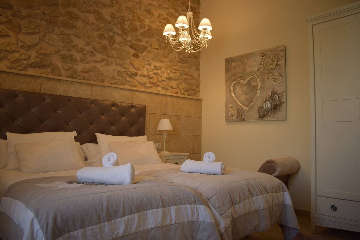 A well-appointed bedroom with a stone wall, a tufted headboard, and a chandelier.