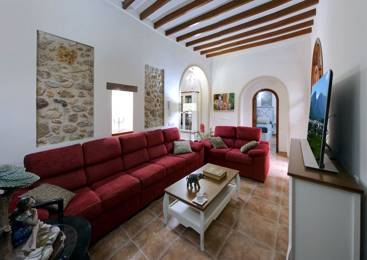 Una sala de estar con sofás rojos, una mesa de centro y un televisor. Se aprecia una pared de piedra y un cuadro colgado.