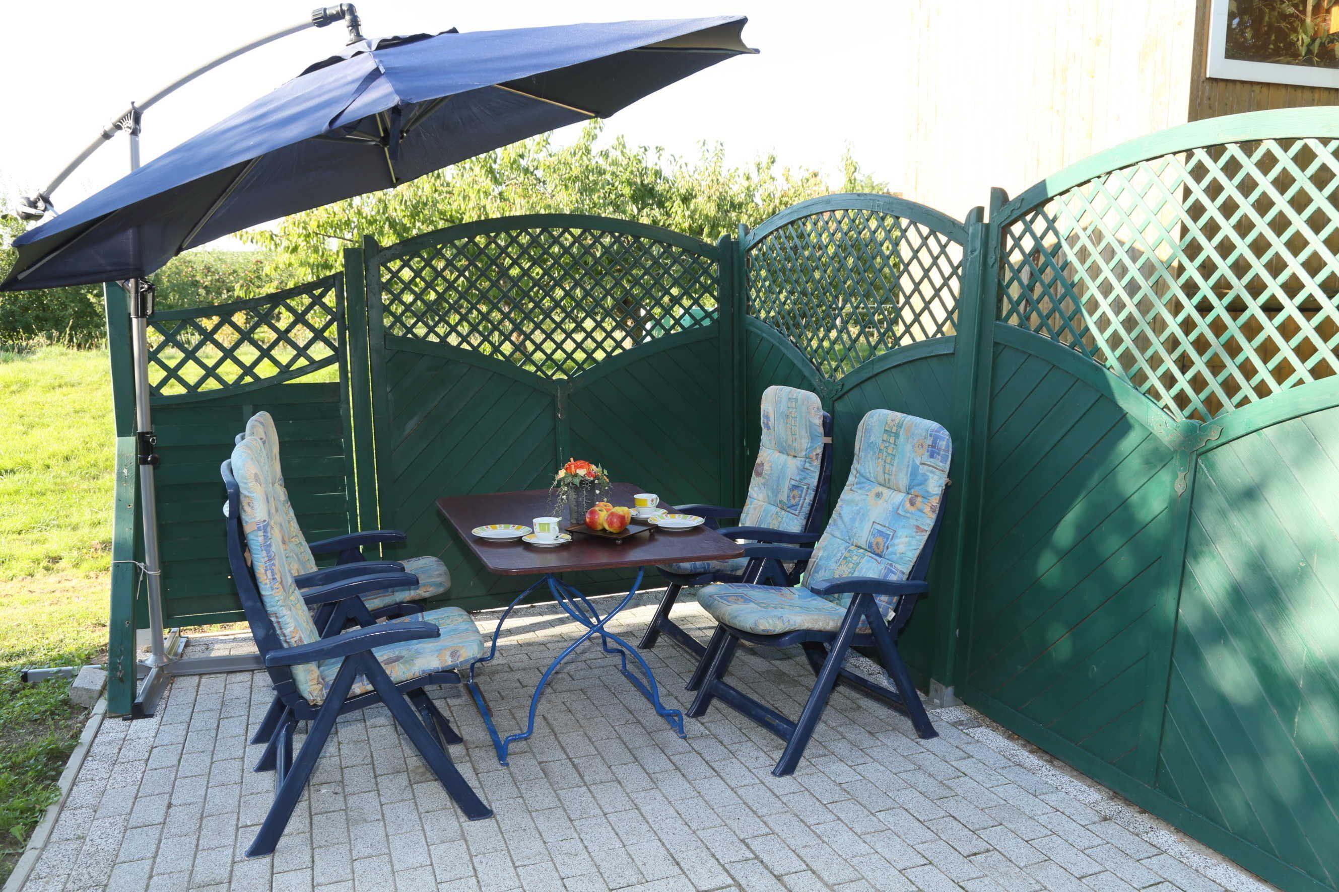Een terras met een tafel en stoelen, een zonnescherm en een groen houten schutting.
