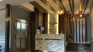A modern hotel lobby with a marble reception desk, an elevator, and a staircase leading to another floor. - New Taksim  (Istanbul)