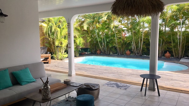 Et moderne udendørs opholdsområde med swimmingpool, sofa og hængende lysarmatur.