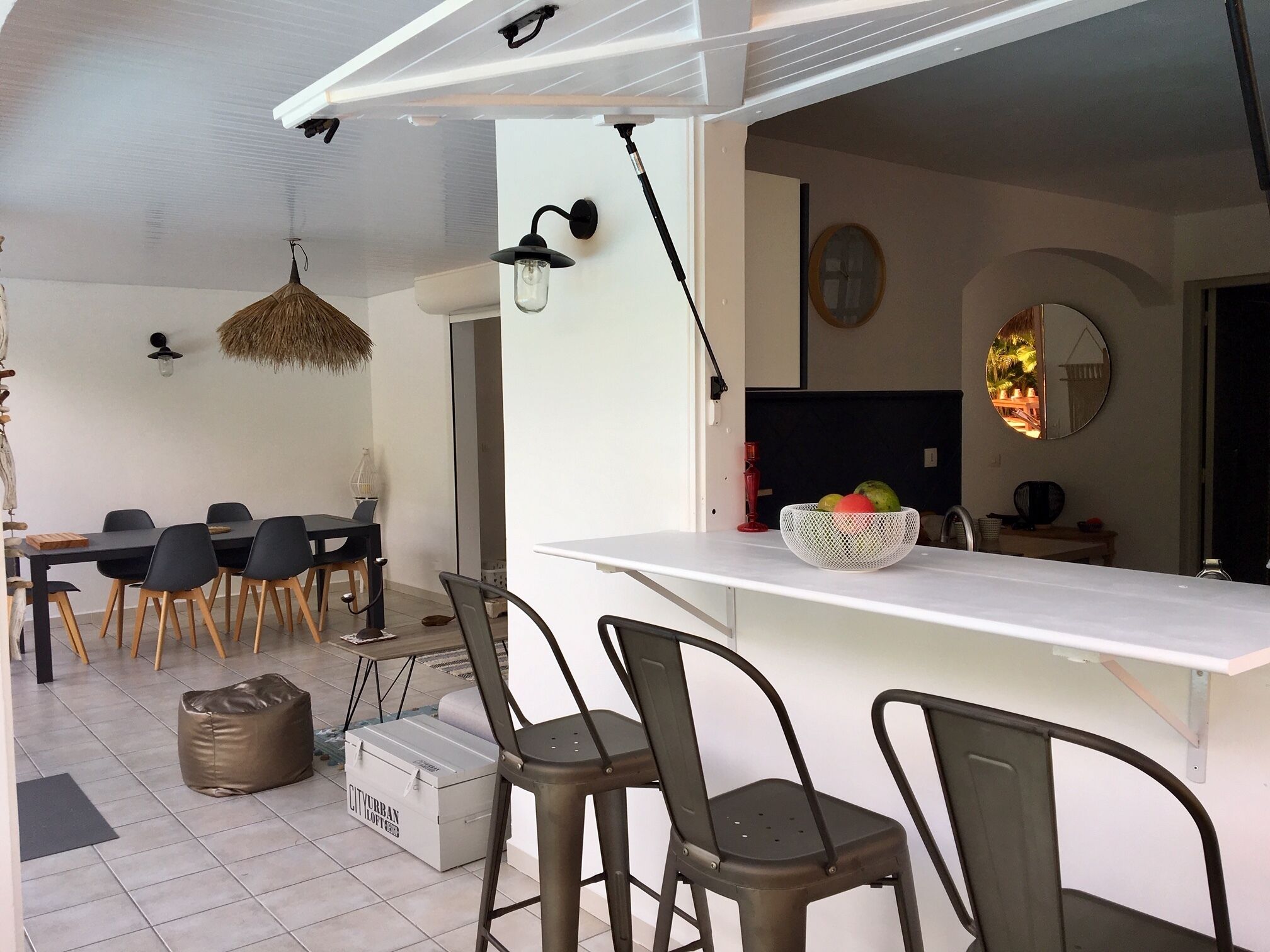 A modern kitchen with a white countertop, black chairs, and a fruit bowl.
