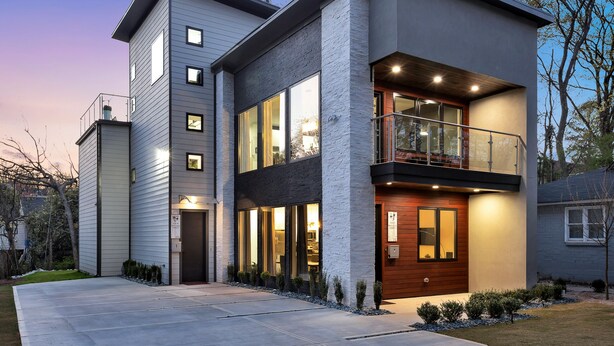 Een modern huis met twee verdiepingen, een balkon, grote ramen en een goed verlichte entree.