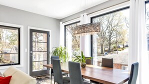 Een moderne eetruimte met een houten tafel en stoelen, grote ramen met uitzicht en een plant in een pot op de tafel.