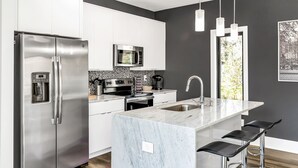 Een moderne keuken met roestvrijstalen apparatuur, een marmeren kookeiland en barstoelen.