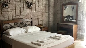 A neatly made bed with white linens and folded towels, a wooden headboard, and a stone-patterned wall with a mirror and wall-mounted lights. - Babylon Gardens Apart Hotel (Menderes)