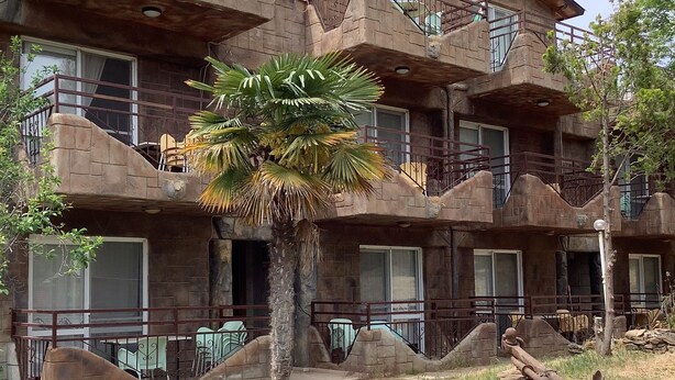 A multi-story building with balconies, a palm tree, and a large clay pot in the foreground. - Babylon Gardens Apart Hotel (Menderes)