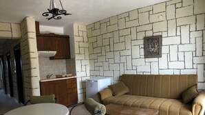 A living room with a sofa, a table, and chairs. There is a kitchen area with cabinets and a refrigerator. - Babylon Gardens Apart Hotel (Menderes)