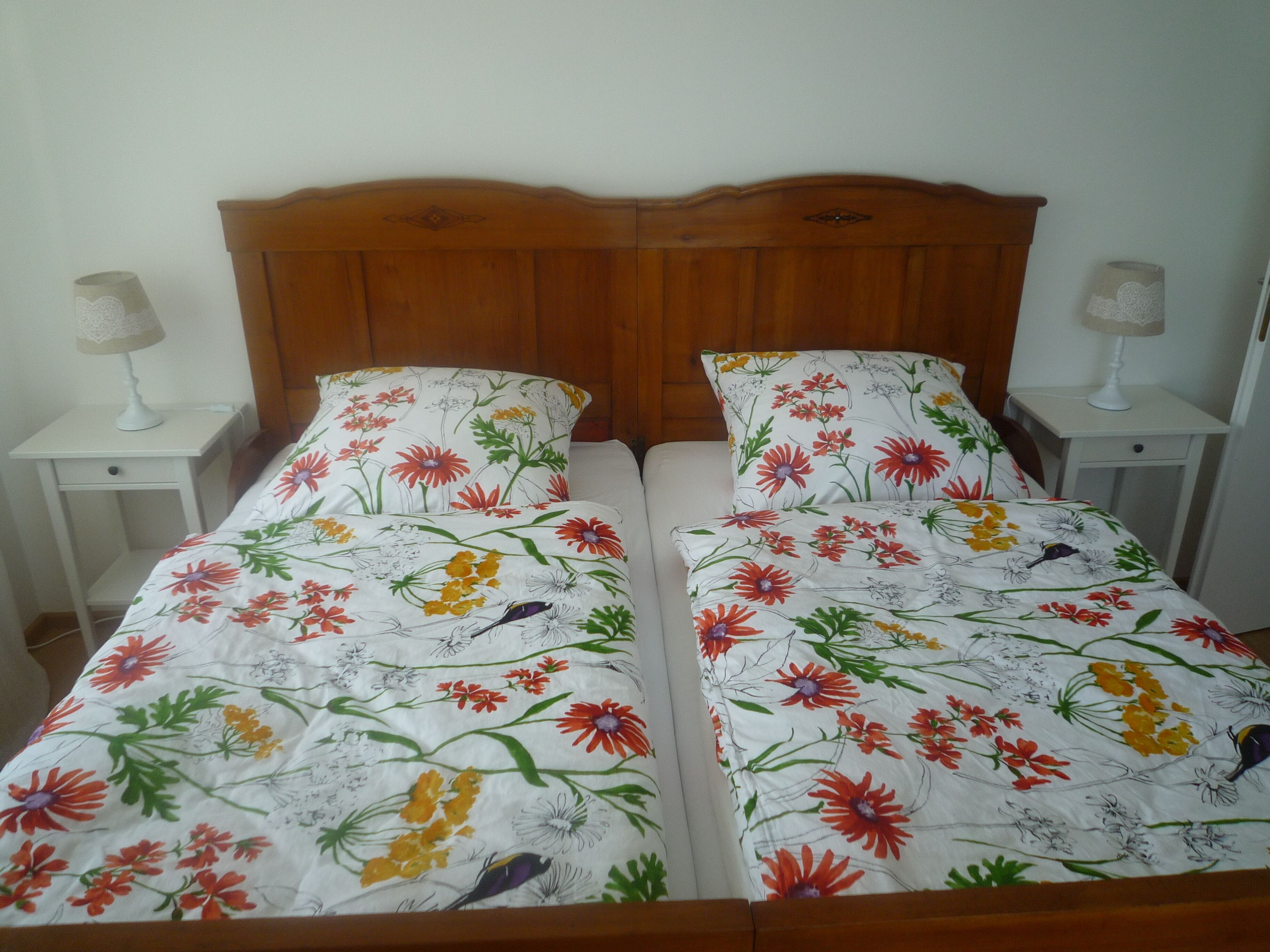 Ein Doppelbett mit floralem Bettbezug, einem hölzernen Kopfteil und Nachttischen mit Lampen.