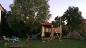 A backyard with a wooden playhouse, a slide, and outdoor furniture.