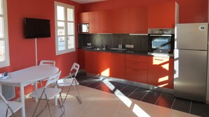 Une cuisine avec des meubles de couleur rouge, un plan de travail noir et un réfrigérateur en acier inoxydable.
