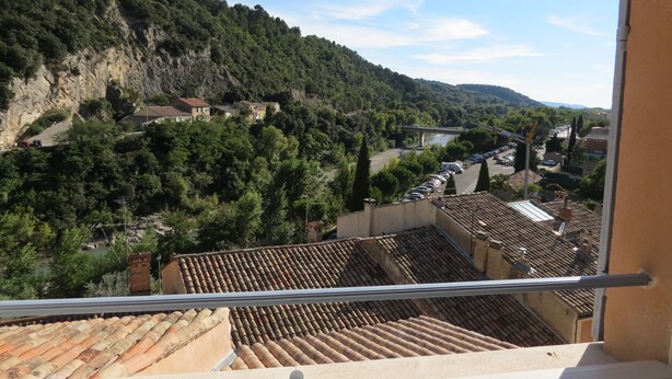 Une vue depuis un balcon donnant sur une vallée, avec des bâtiments en terrasses, un pont et un parking.