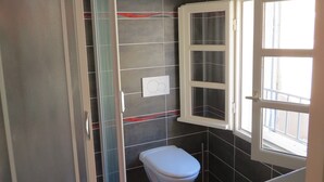 Une salle de bain comprenant des toilettes, un espace douche et une fenêtre.
