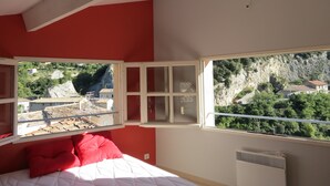 Une chambre à coucher avec un lit, des oreillers rouges, une fenêtre donnant sur un paysage montagneux et un radiateur blanc.