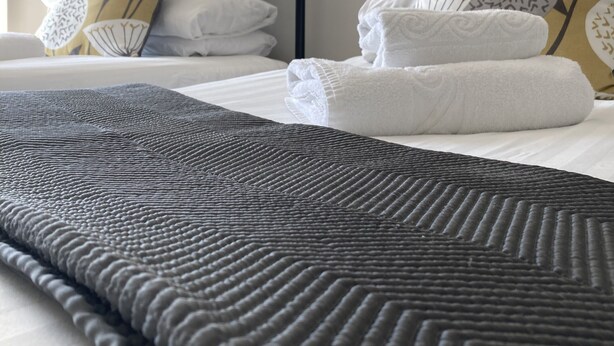 A neatly made bed with a dark textured blanket, white pillows, and a floral-patterned headboard. - Old Temperance House (Helston)