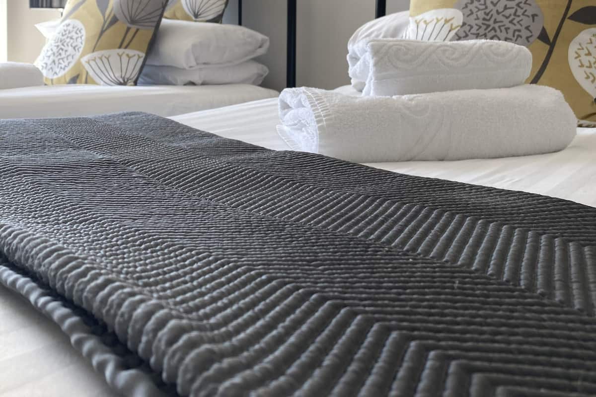 A neatly made bed with a dark textured blanket, white pillows, and a floral-patterned headboard.