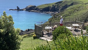 A coastal terrace with a view of the sea and cliffs, featuring outdoor seating and a wooden fence. - Old Temperance House (Helston)
