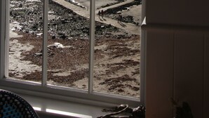 A view through a window of a beach with a rocky shoreline, a sandy beach, and a hill in the distance. - Old Temperance House (Helston)