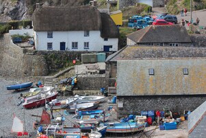 Un pueblo costero con casas de techo de paja, un muro de piedra y varios barcos amarrados a la orilla.
