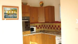 A compact kitchen with wooden cabinets, a microwave, a washing machine, and a dining area with a wooden table and chairs. - Studio 25 M2, air-conditioned 350mt from the beach. (Hyères)