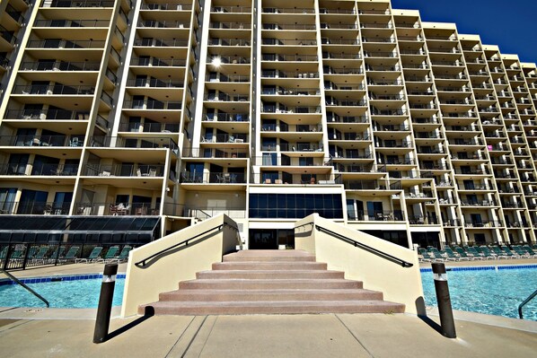 A multi-story hotel with a pool area, featuring a staircase leading to the pool, and balconies on each floor.