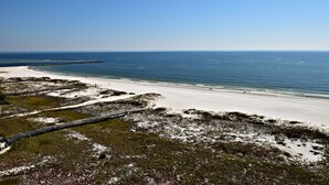 Ein Strand mit einer Holzpromenade, die zum Ufer führt, feinem Sand und dem Meer.