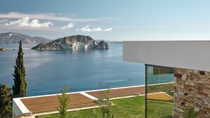 A modern building with a large glass window overlooking a calm sea and distant mountains. - Alkyonides Villas (Zakynthos)