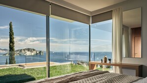 A bedroom with a large window overlooking a scenic view of a coastline and greenery. - Alkyonides Villas (Zakynthos)