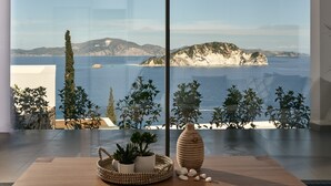 A modern interior with a large window overlooking a coastal landscape. - Alkyonides Villas (Zakynthos)