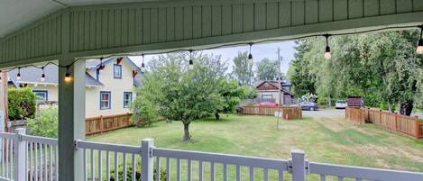 A covered porch with a white railing, a lawn, and a wooden fence.