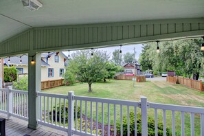 Een overdekte veranda met een witte balustrade, gazon en houten omheining.