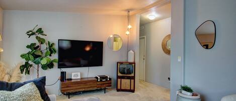 Una sala de estar con una televisión de pantalla plana, un mueble de madera, una planta en maceta y un espejo redondo en la pared.
