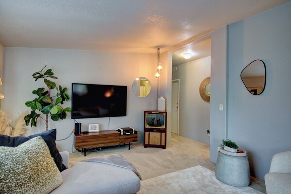 Een woonkamer met een flatscreen televisie, een houten kast, een potplant en een ronde spiegel aan de muur.