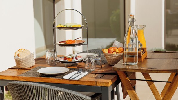 A breakfast table set with bread, pastries, and a fruit plate, along with a bottle of orange juice and glasses. - Casa Rural Canelobre (Busot)