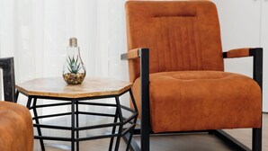 A modern room with a round wooden table, a glass vase with a plant, and an orange chair with black metal legs. - Casa Rural Canelobre (Busot)