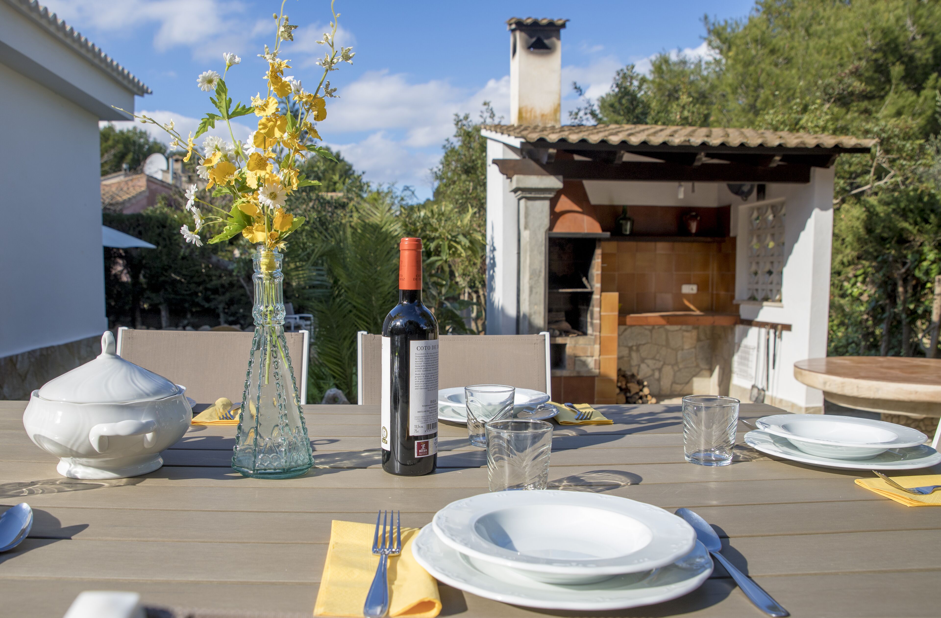 A dining table set with plates, cutlery, a wine bottle, and a vase of flowers.