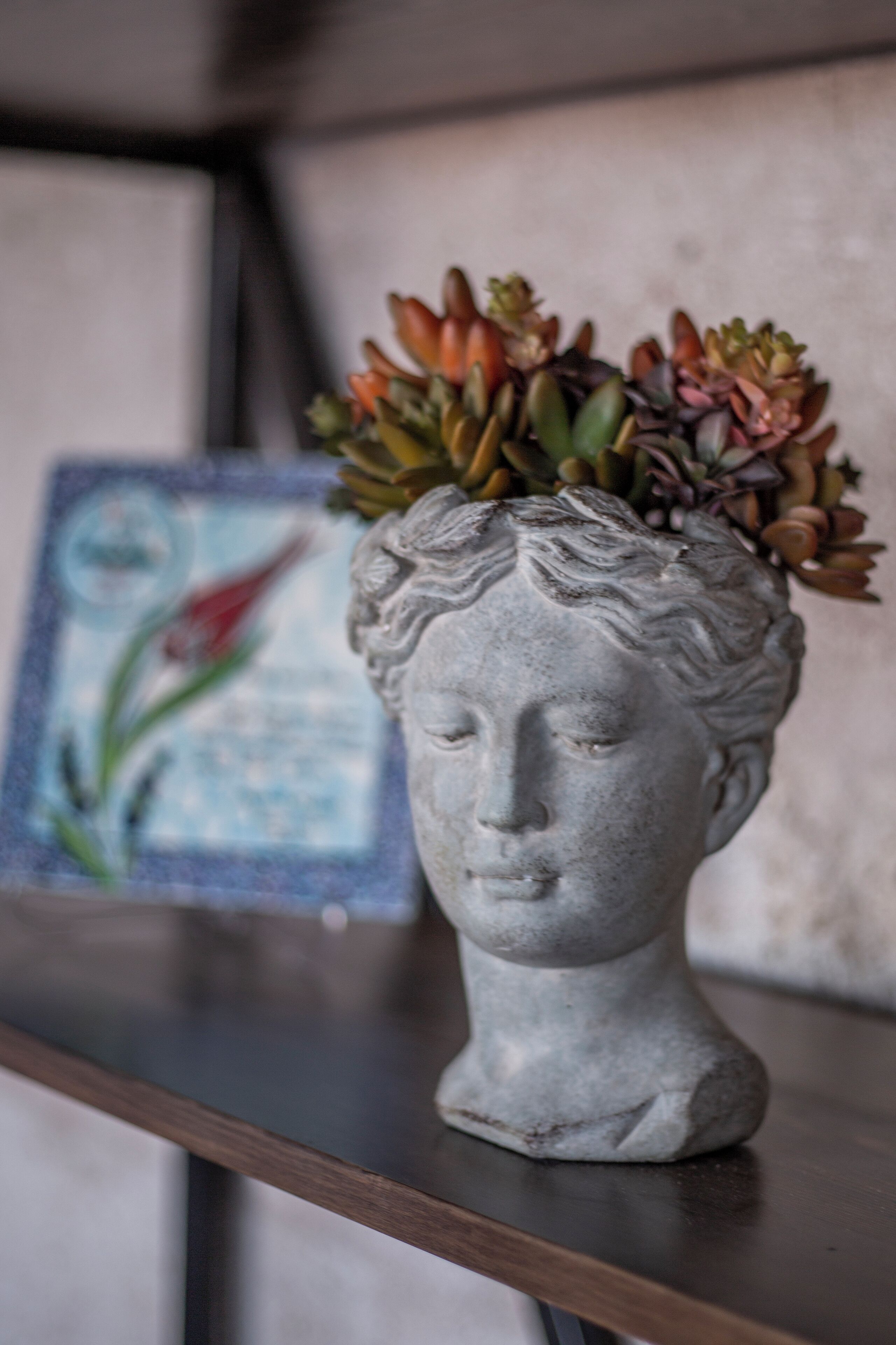 Un busto de piedra con un arreglo floral sobre una estantería.