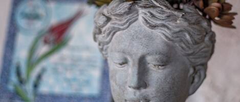 Un busto de piedra con un arreglo floral sobre una estantería.