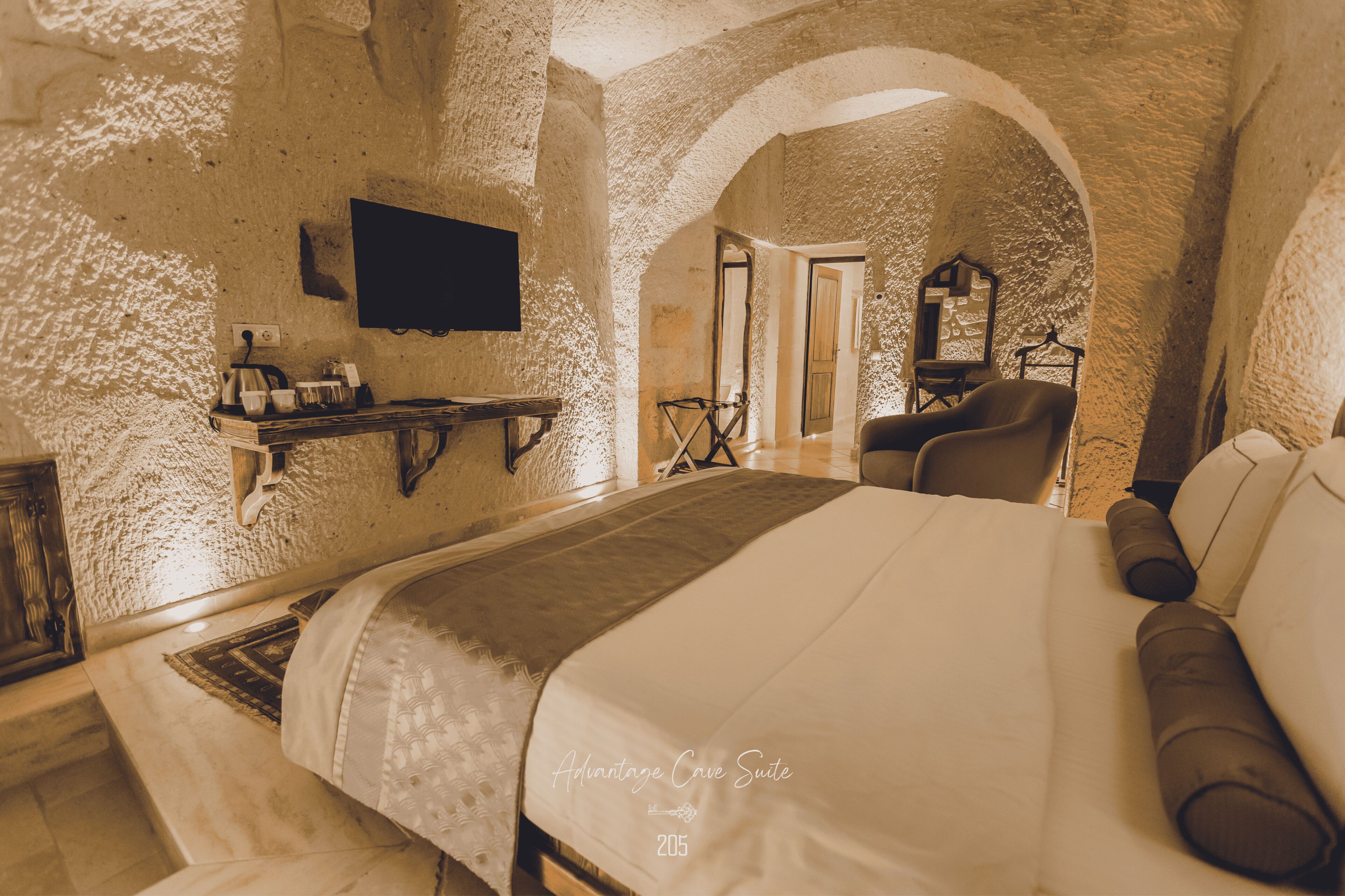 A hotel room with a large bed, a mounted TV, a small table with a lamp, and a chair.