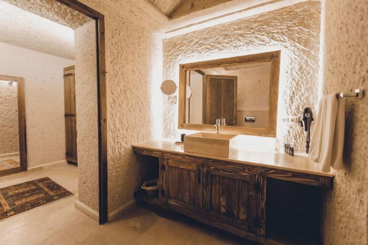 Un baño con pared de piedra, tocador de madera, espejo grande y lavamanos.