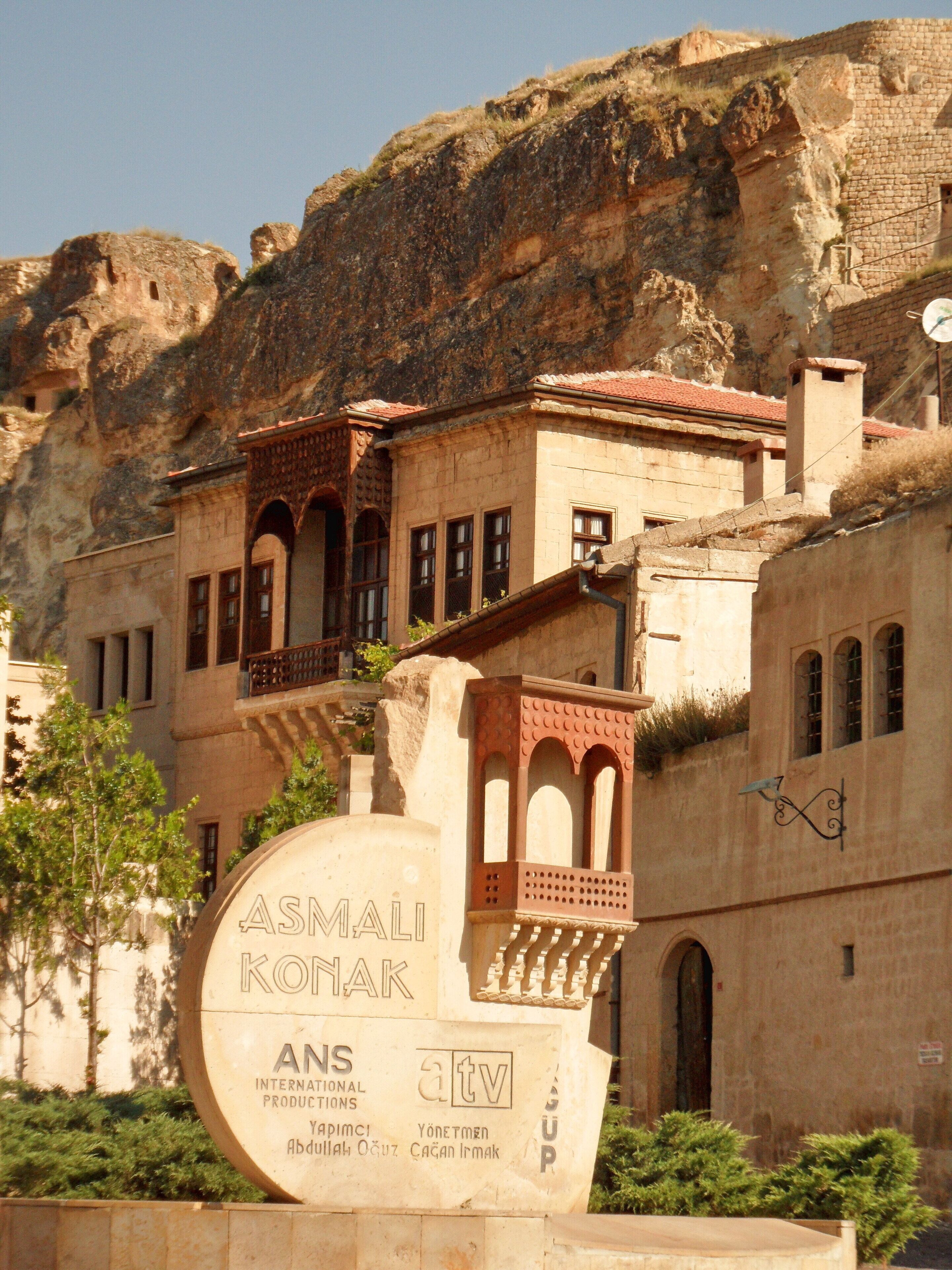 Un bâtiment à la façade en pierre et aux fenêtres en arc de cercle, sur lequel on peut voir une enseigne avec les inscriptions « ASMAKI KOMAK » et « ANS INTERNATIONAL PRODUCTIONS ».