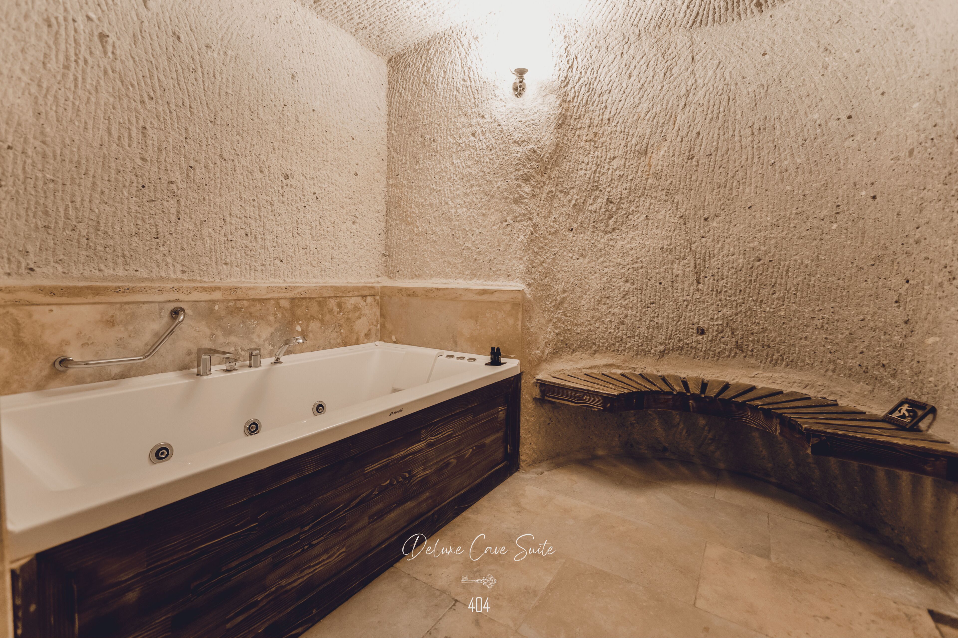 Un baño con una bañera grande, un tocador de madera y una pared de piedra texturizada.
