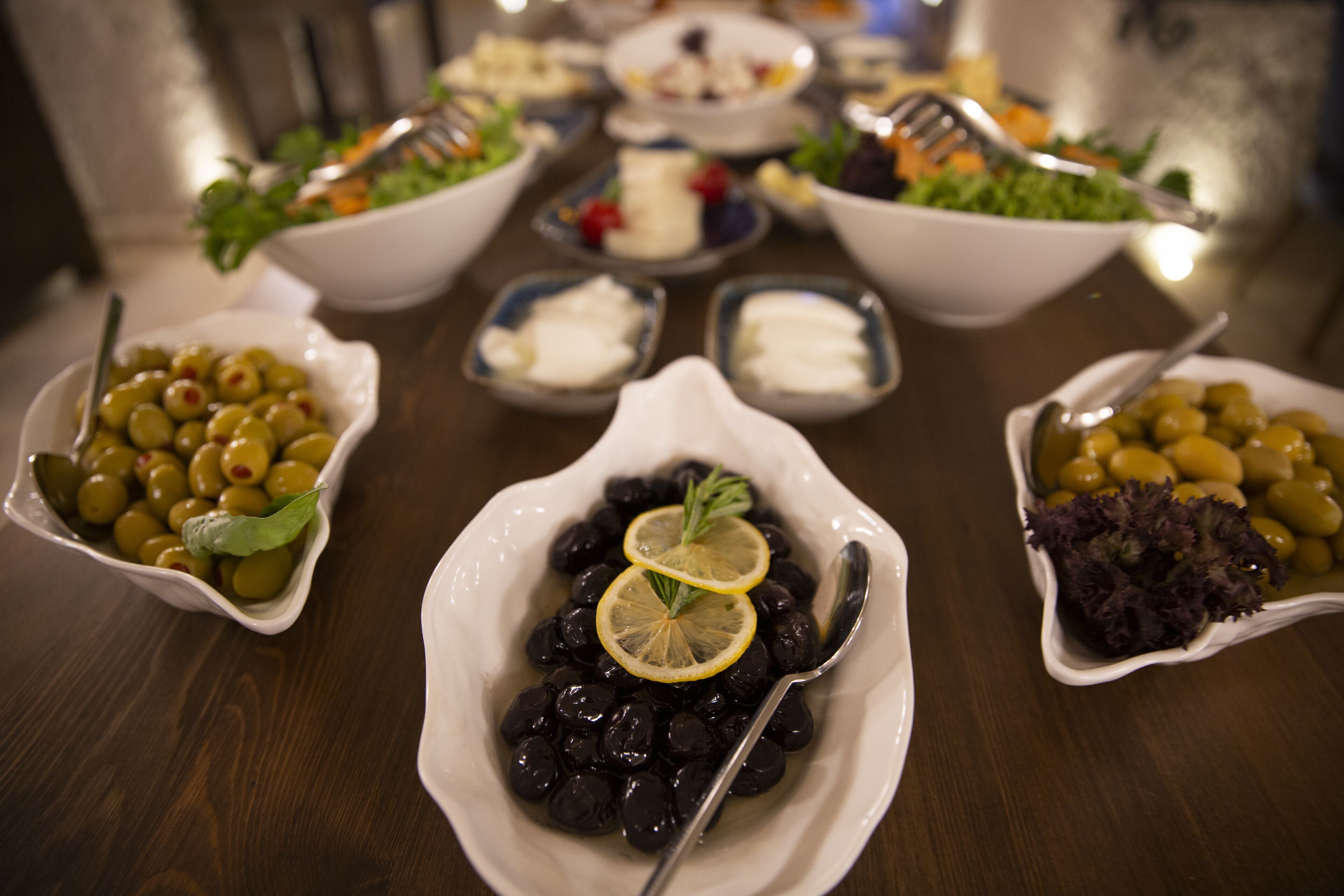 A table with various dishes, including olives and salads, arranged for a meal.