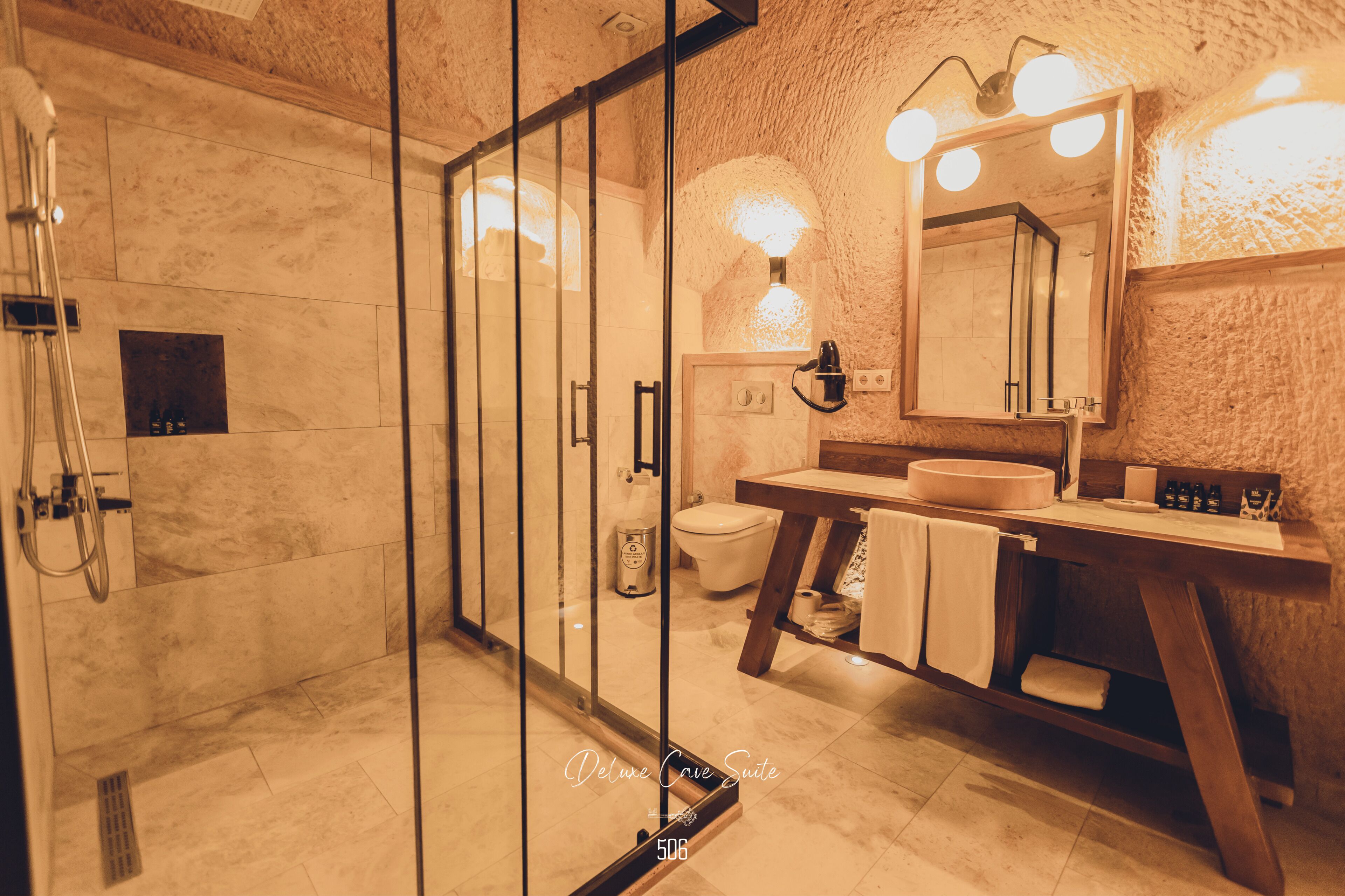 A modern bathroom with a glass shower enclosure, a wooden vanity, and a large mirror with lights.