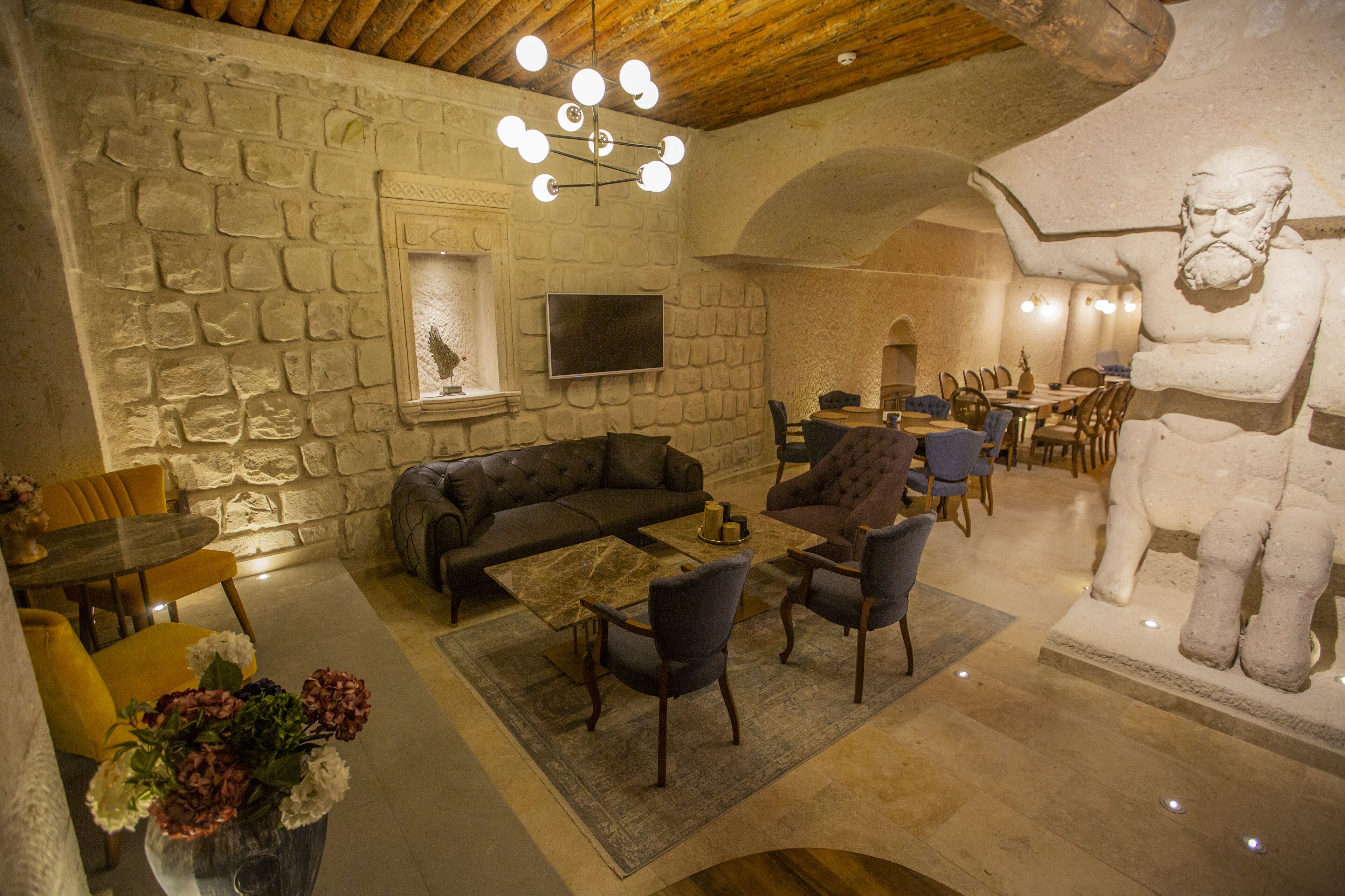 A stone-walled room with a sofa, armchairs, a TV, and a large statue.