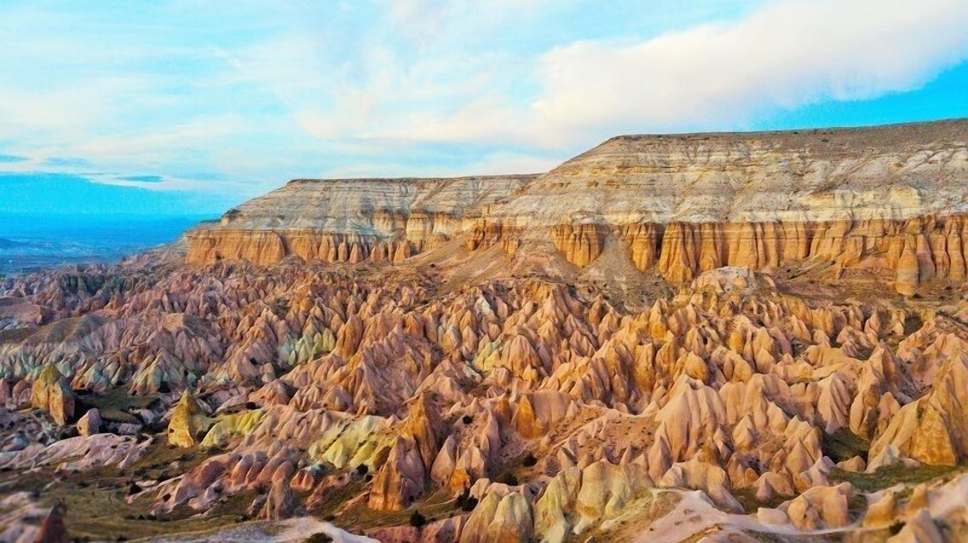 Vista panorâmica de uma paisagem acidentada com formações rochosas em camadas e um horizonte com edifícios da cidade ao longe.