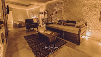 A cozy living room with a sofa, armchair, and coffee table, featuring a rustic stone wall and a patterned rug.